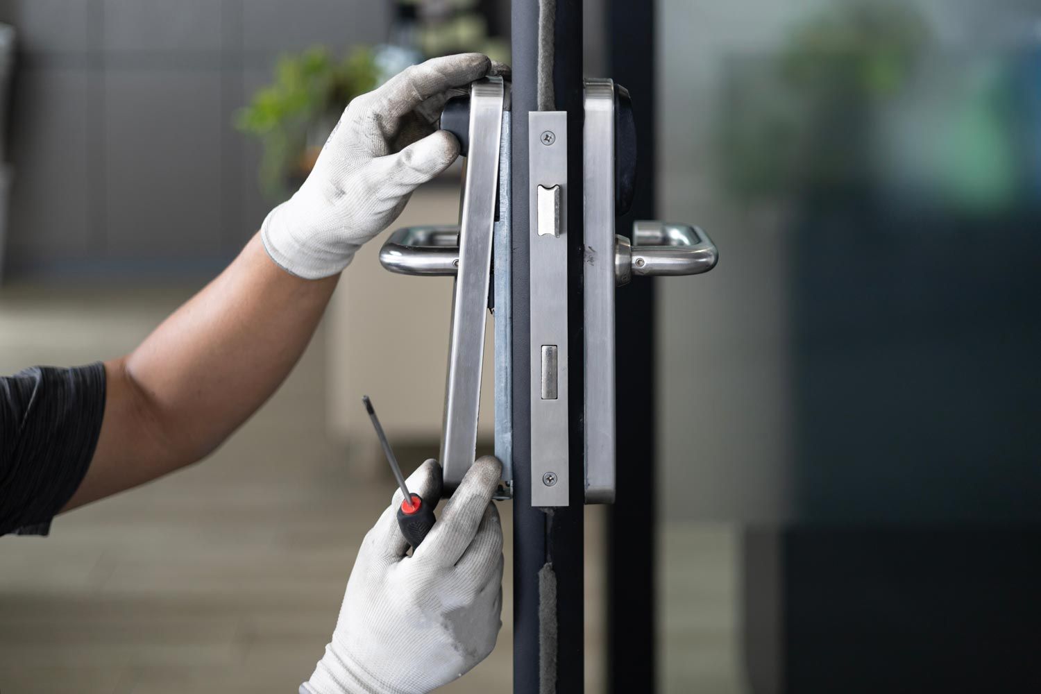 Gloved hands opening a glass door with a red screwdriver near the lock.