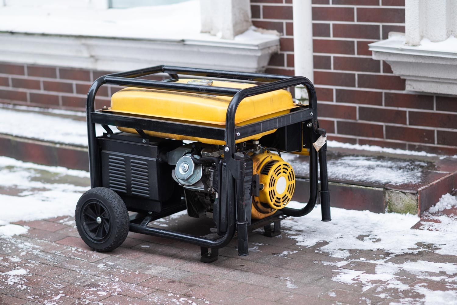 Yellow portable generator on a snowy porch beside a brick wall