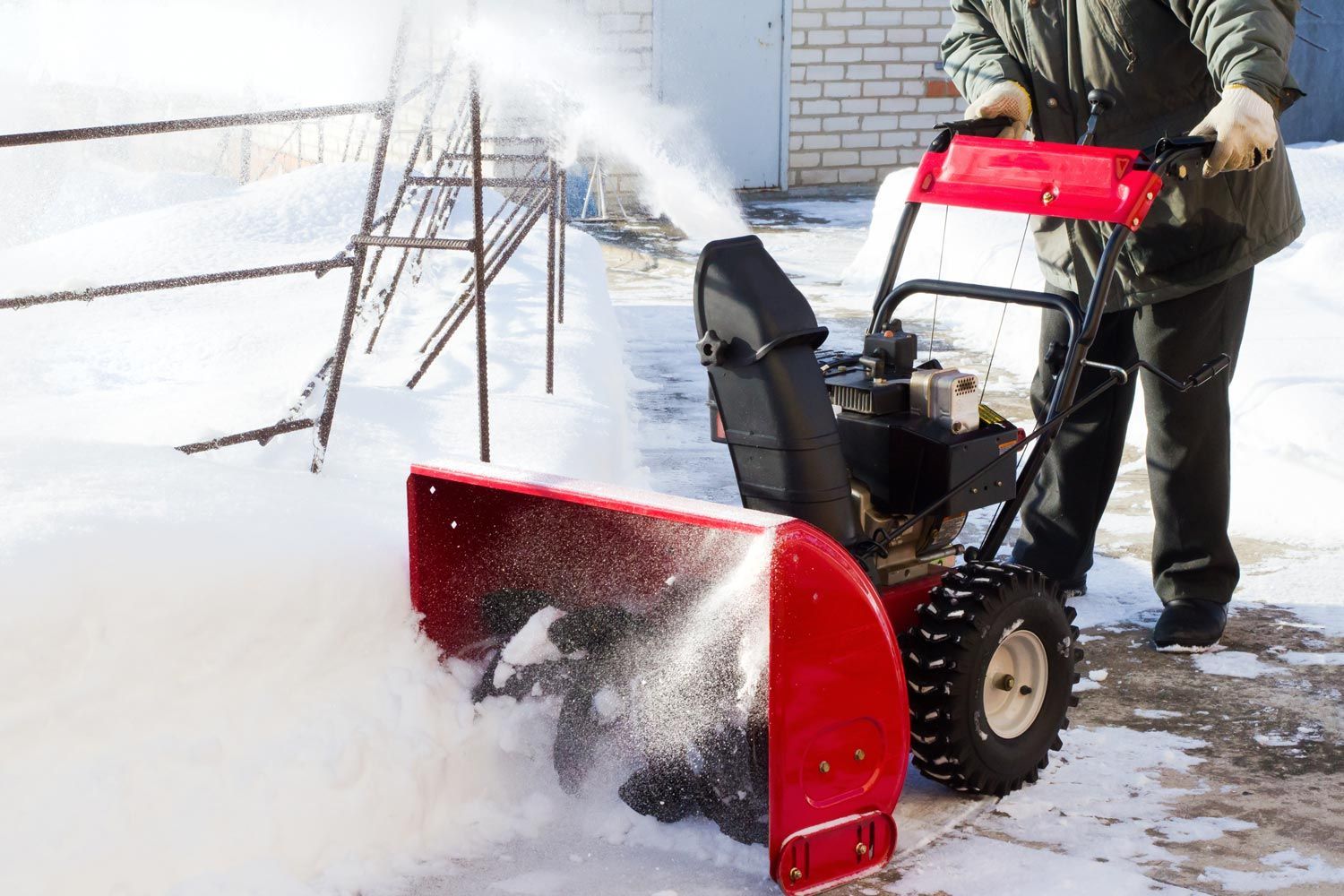 Person using a red snow blower to clear snow from a driveway
