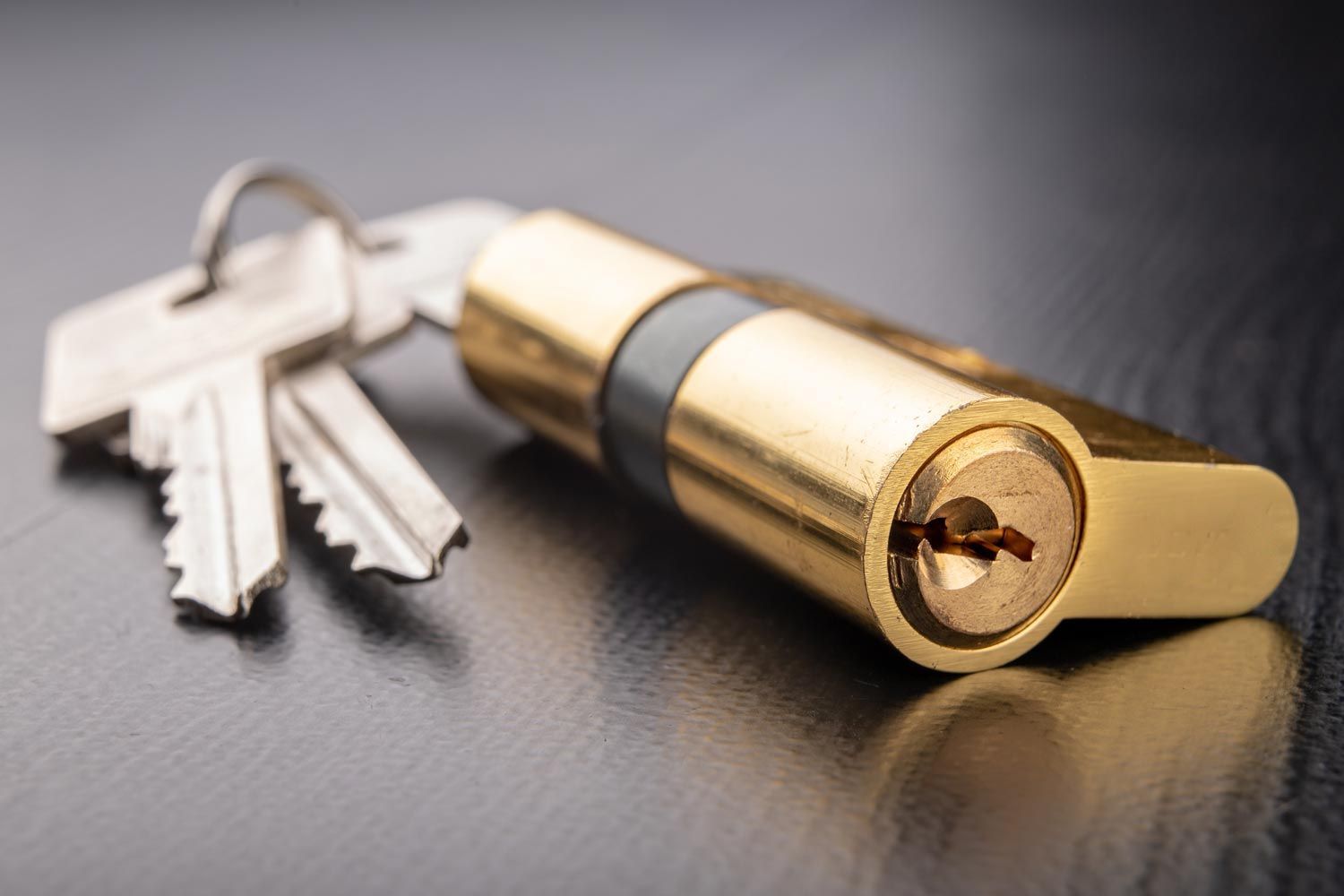 Golden door lock with two silver keys on a dark surface