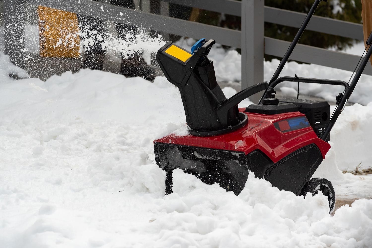 Red snowblower clearing thick snow beside a wooden fence