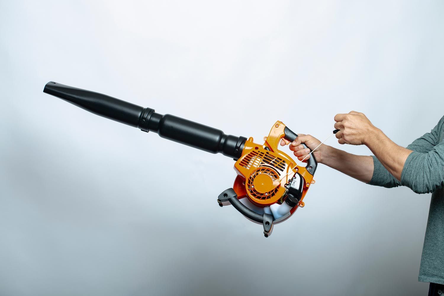Handheld orange leaf blower with black nozzle, held by a person against a plain gray background