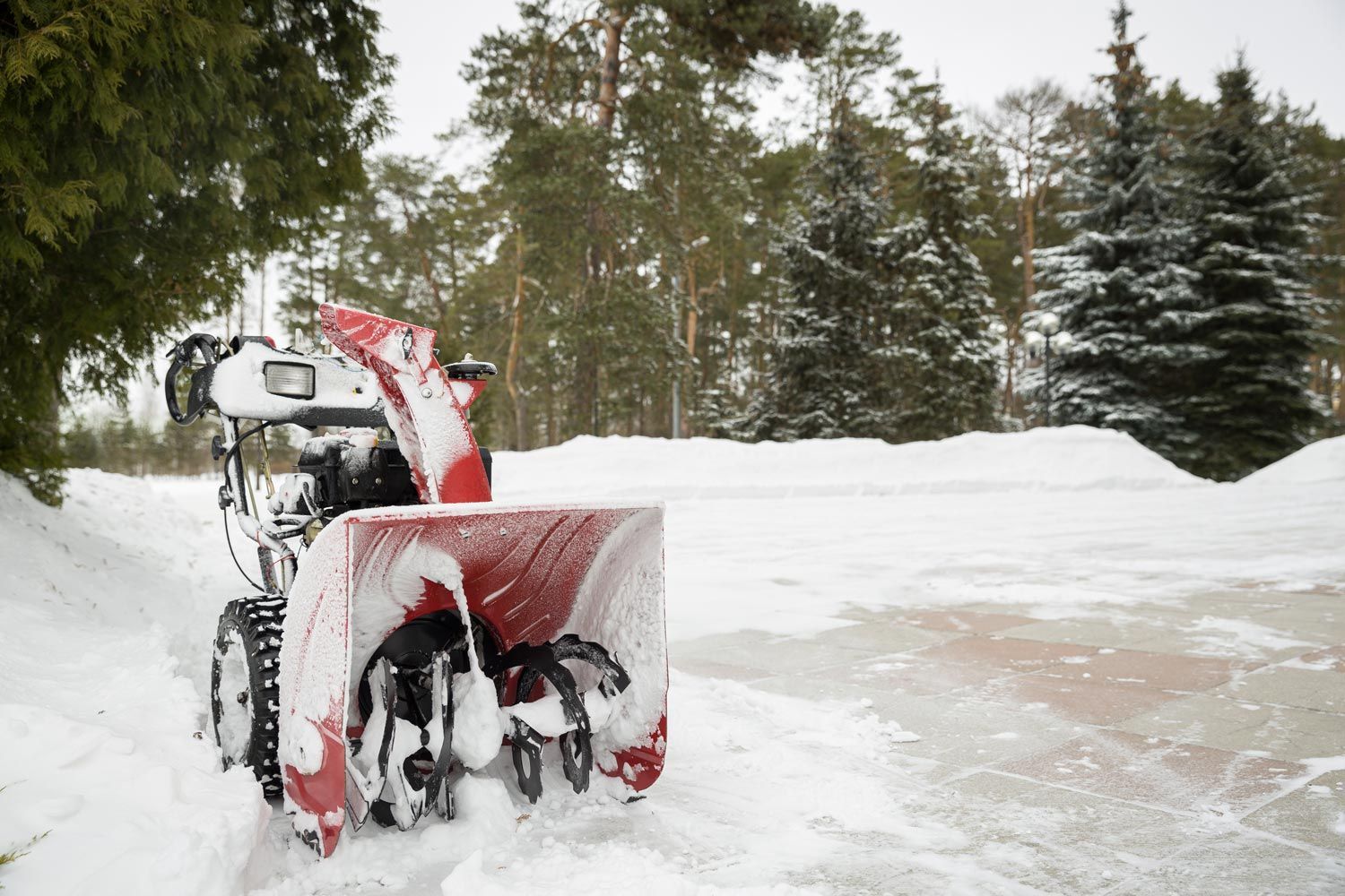 Snowblower clearing a snowy driveway, with snow piled around the red machine and trees in the background