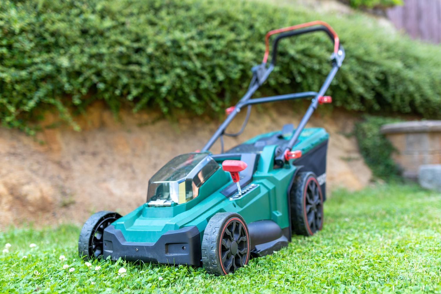 Green lawn mower on grass outdoors, with teal body, black wheels, and a red handle.