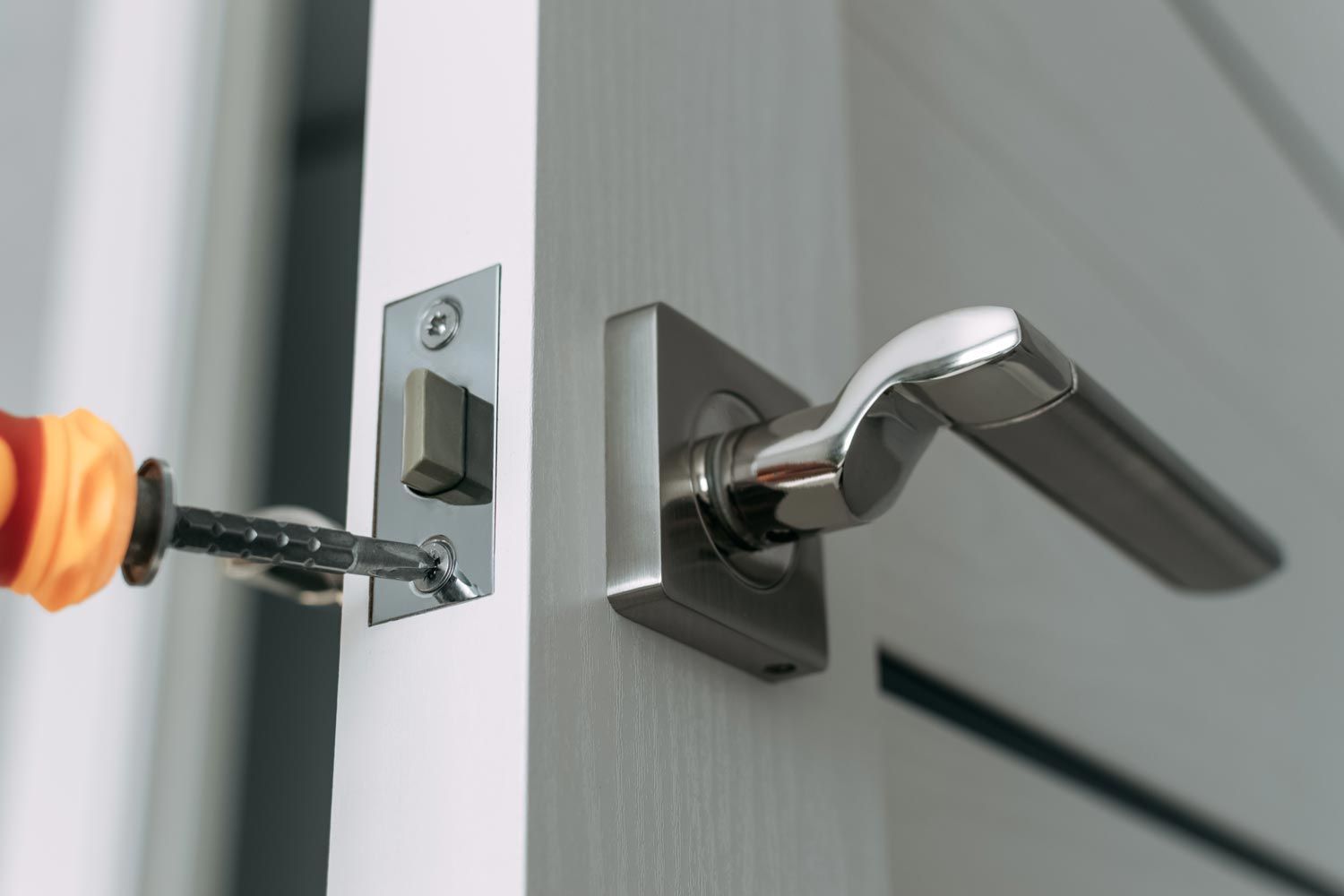 Screwdriver adjusting a strike plate on a door latch with a silver handle