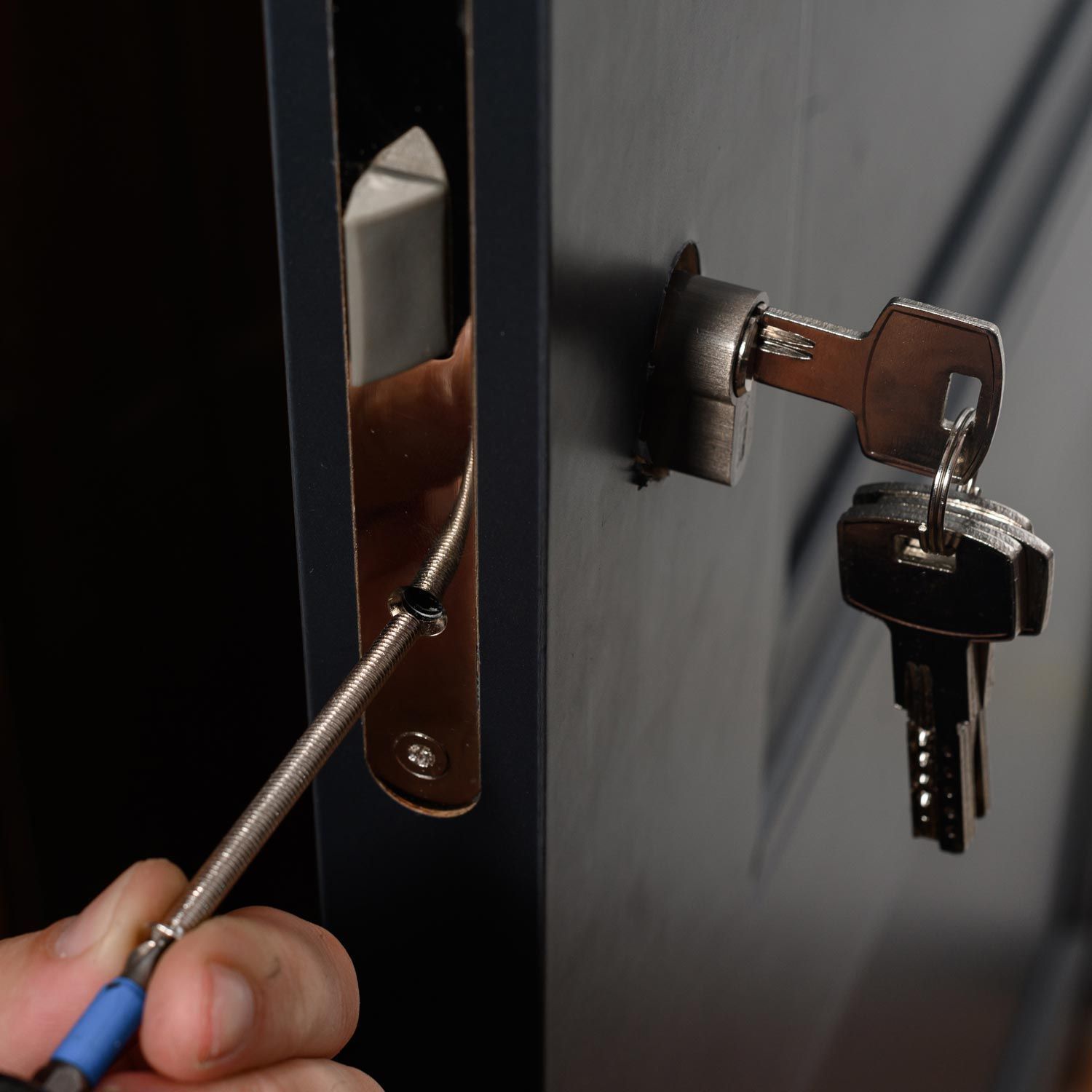 Person using a screwdriver to adjust a door lock with keys in the keyhole.