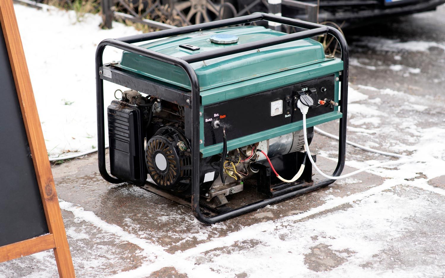 Portable generator on a snowy outdoor surface, green and black with exposed wheels and frame