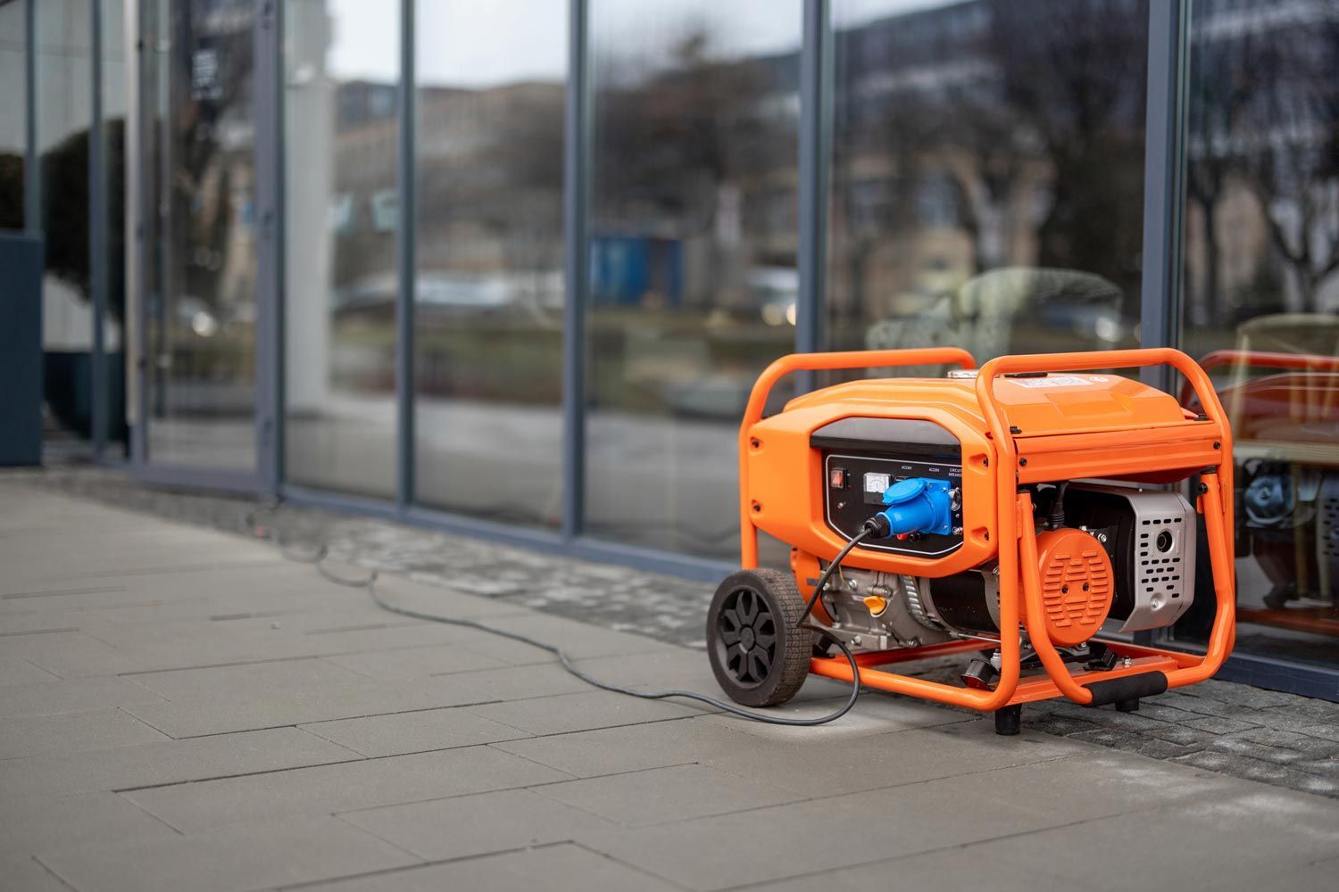 Orange portable generator on a sidewalk beside a glass building