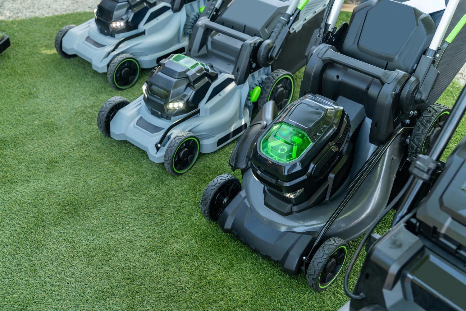 Row of robotic lawn mowers on grass, mostly gray with green accents and glossy black tops