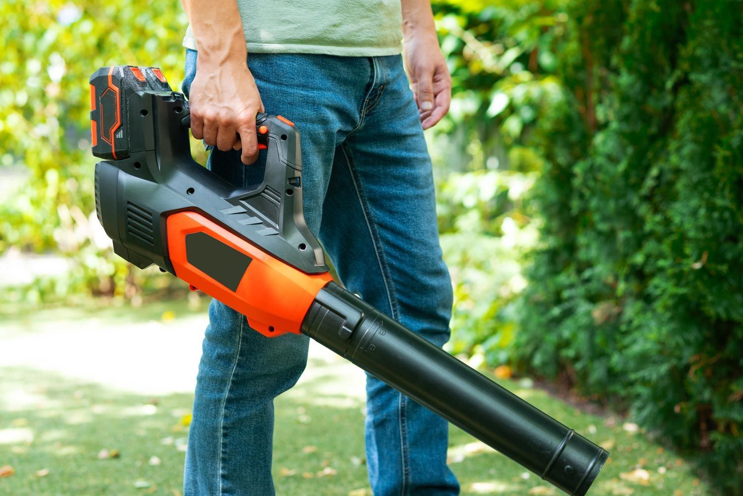 Person holding a black and orange leaf blower outdoors in a green yard