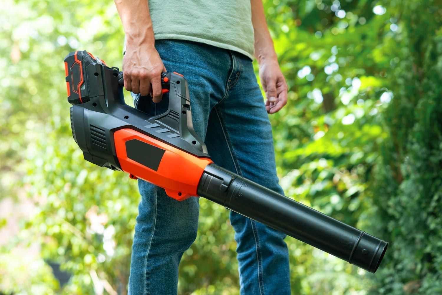 Person holding a black and orange leaf blower outdoors in a grassy area