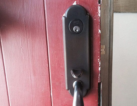 Black door lock and handle on a red wooden door frame.