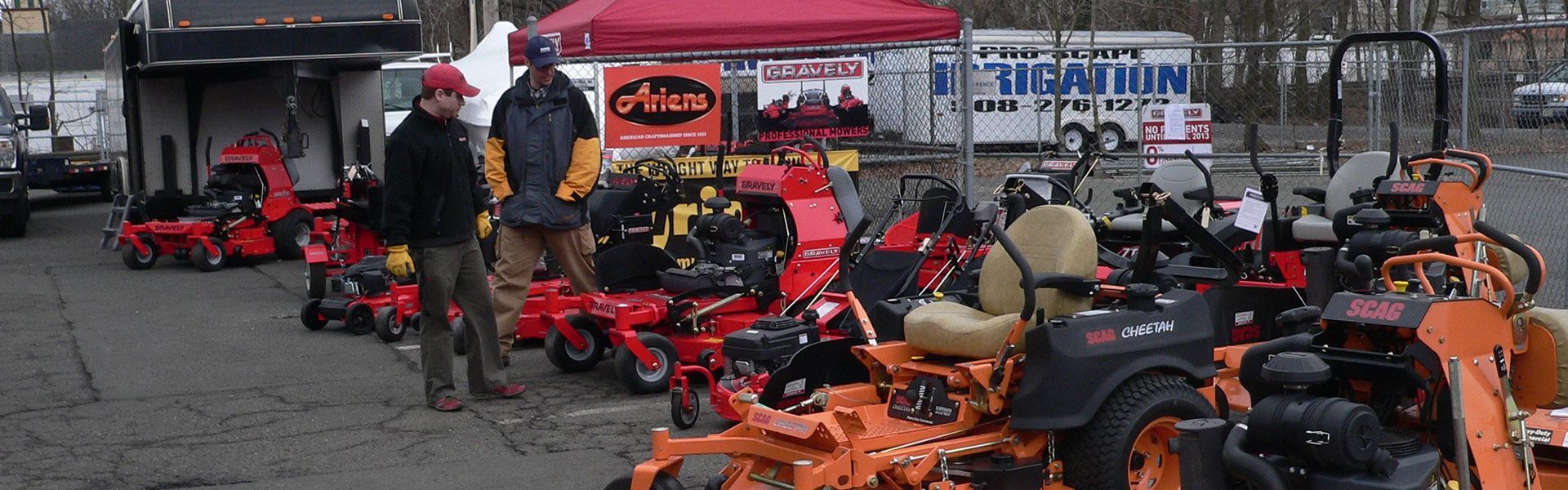 People gathered around rows of red and orange go-karts at an outdoor track booth.