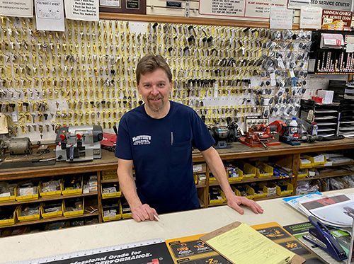 Man standing behind a counter in a hardware store, with tools displayed on the wall behind him.