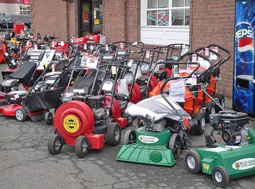 Row of red and green lawn mowers displayed outside a store