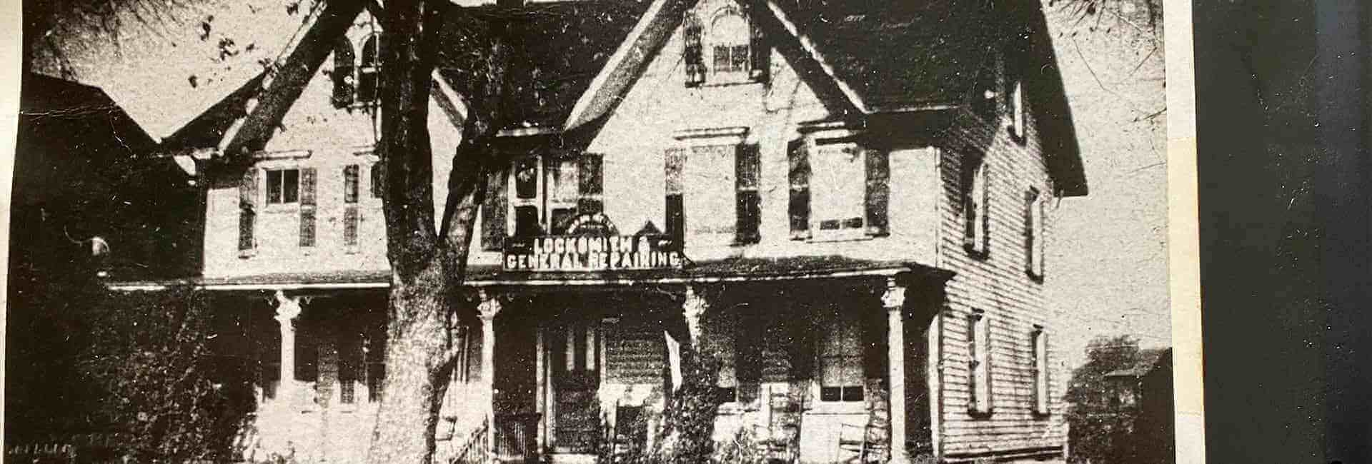 Old black-and-white photo of a large Victorian house with a front porch and steep gables
