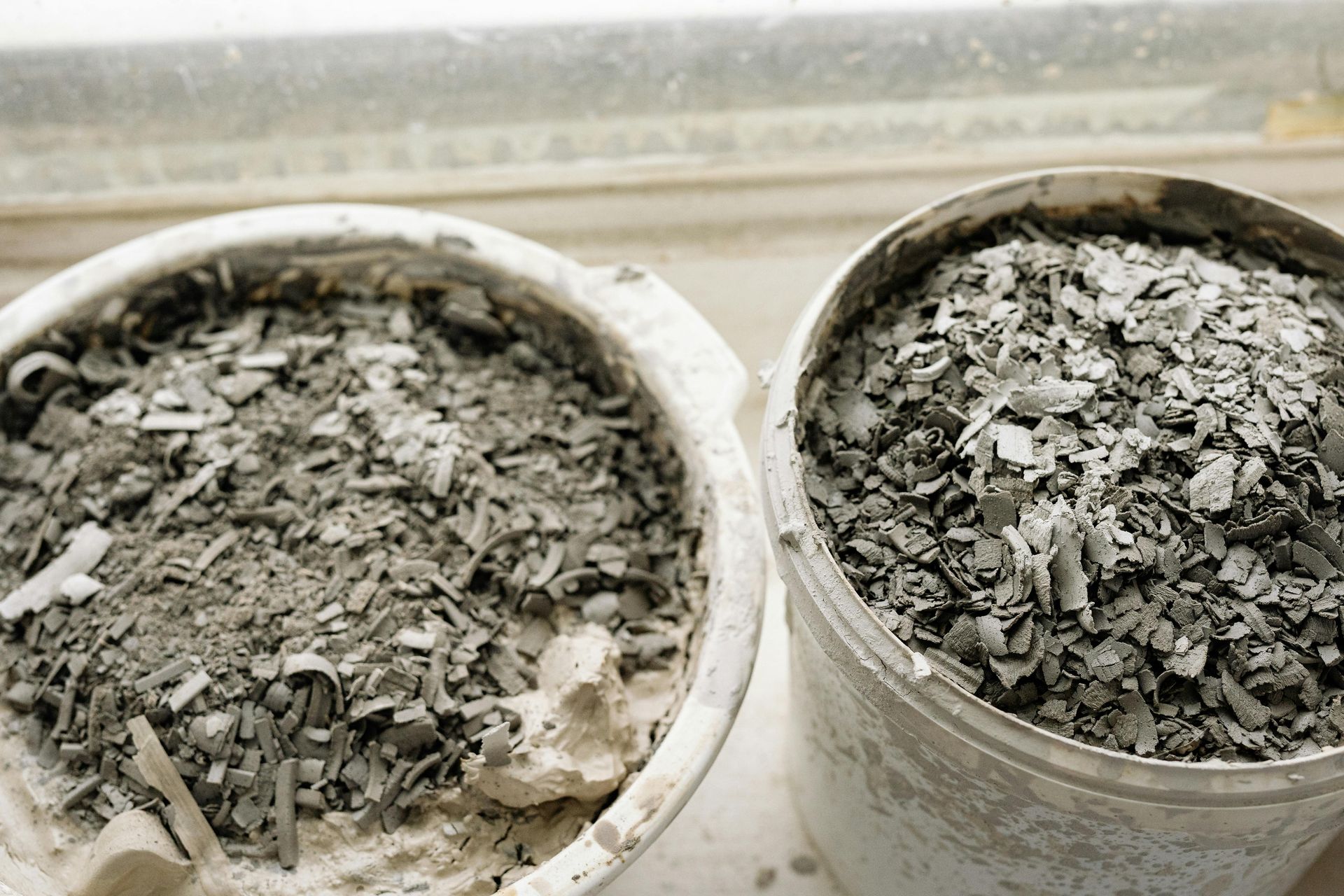 Two gray buckets filled with ash, set near a window.
