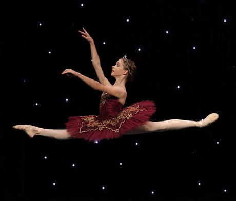 Ballet dancer in a red tutu performing a full split leap against a starry black backdrop