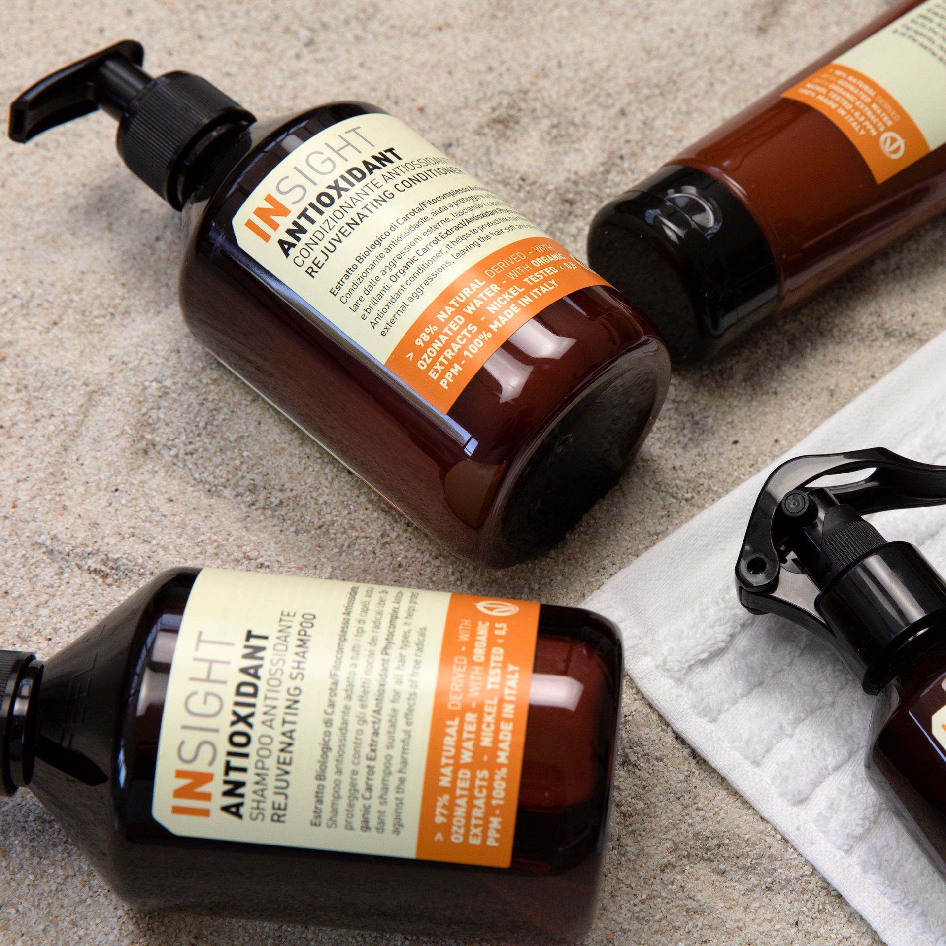 Flaconi con dosatore a pompa marroni di prodotti per la cura dei capelli Insight Antioxidant su una superficie di pietra, uno su un panno bianco.