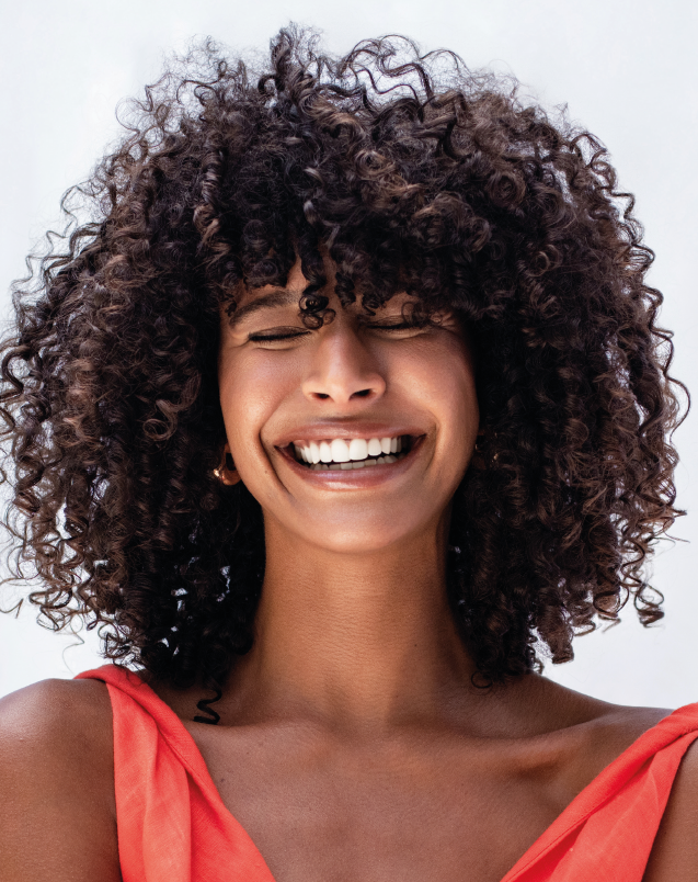 Persona sorridente con i capelli ricci, che indossa una maglietta color corallo su uno sfondo chiaro.
