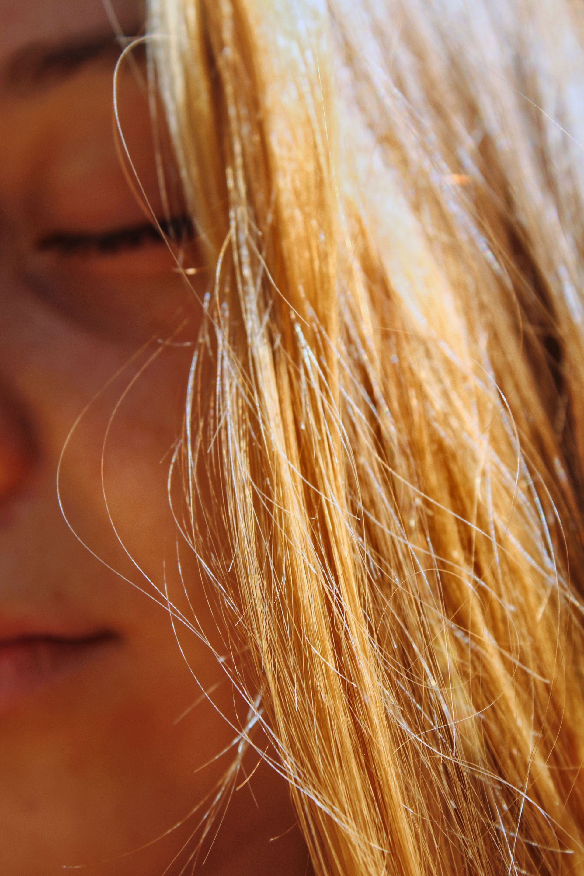 Primo piano del volto di una persona con gli occhi chiusi e i capelli biondi illuminati dal sole che lo coprono parzialmente.