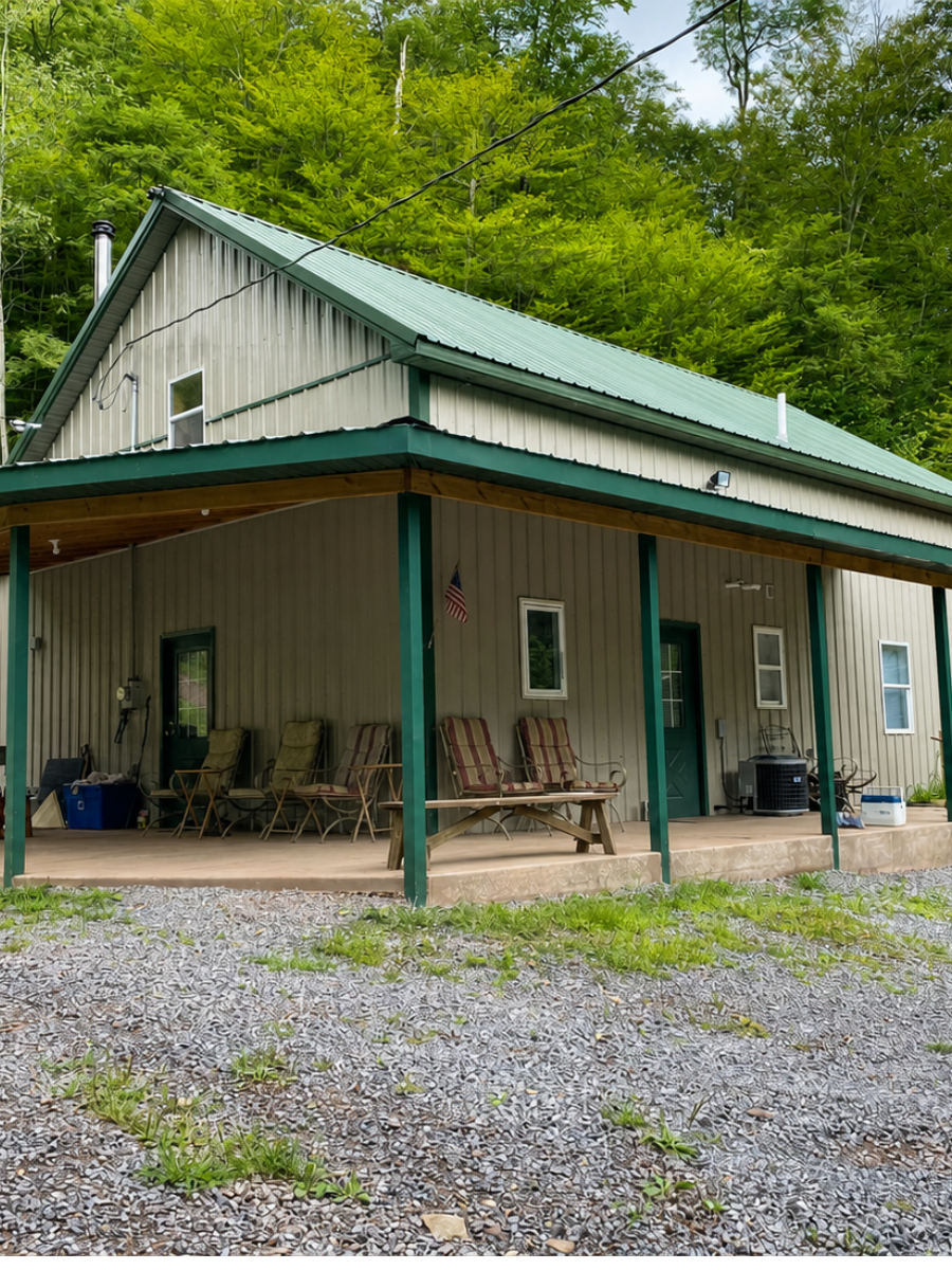 Rustic cabin with green metal roof and porch, surrounded by trees and gravel.