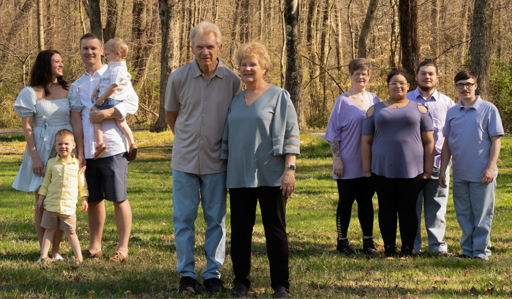A family group standing together outdoors in front of tall trees, some smiling at the camera.