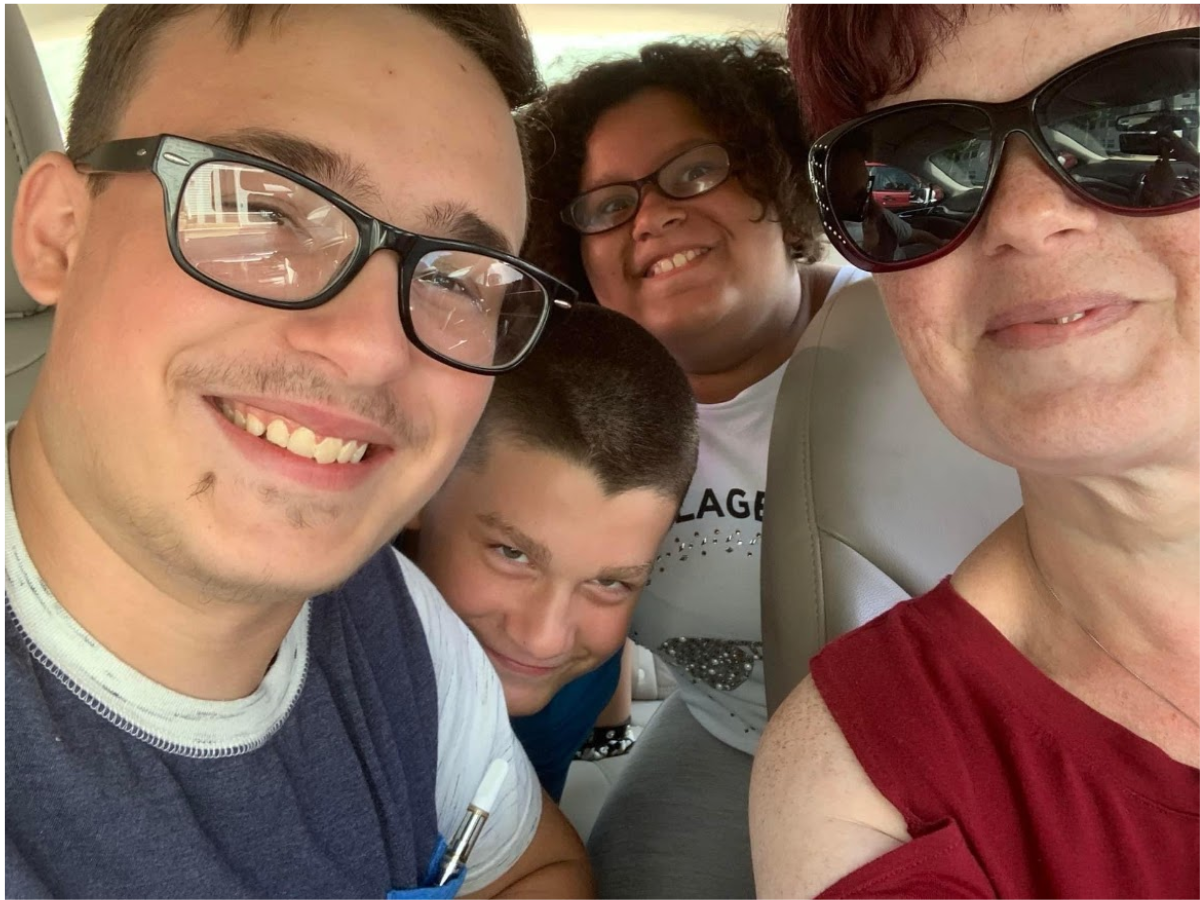 Four smiling people posing closely for a selfie indoors, with glasses and casual clothing.