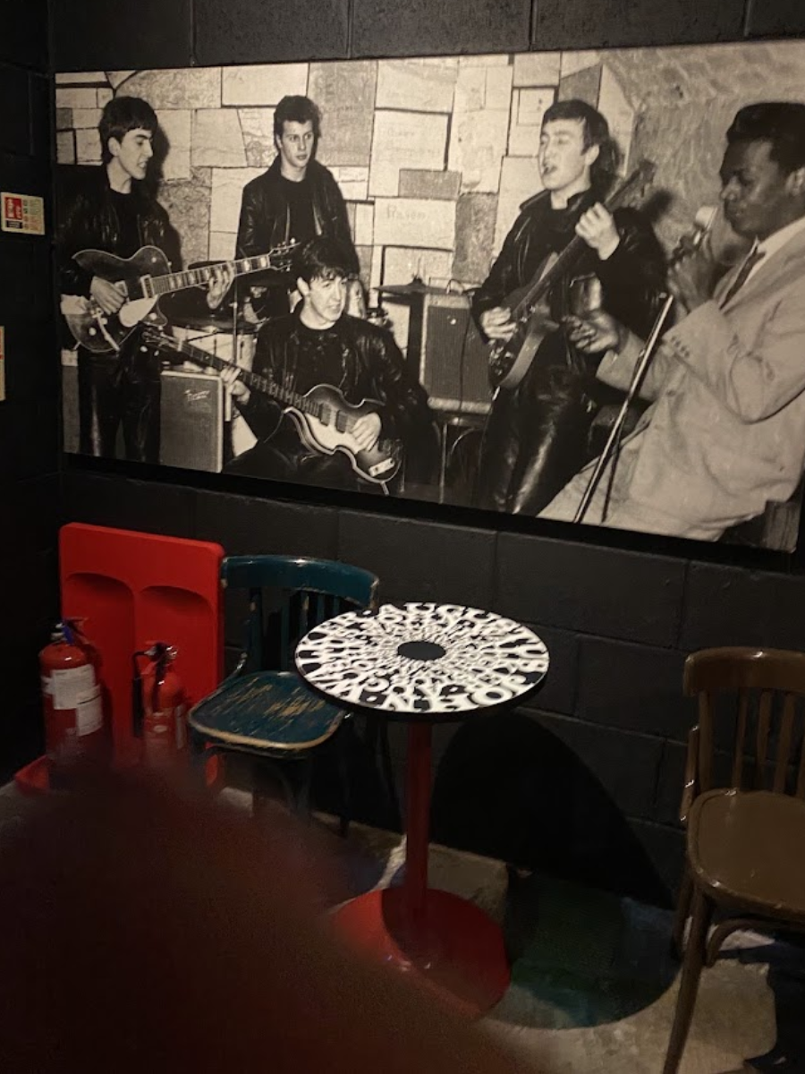 Black-and-white mural of musicians playing in a club, above red and teal chairs and a small table
