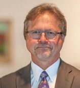 Man with glasses and grey hair in a suit, looking at the viewer.