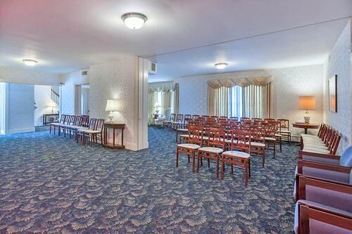 Funeral home chapel with rows of chairs, carpeted floor, and soft lighting.