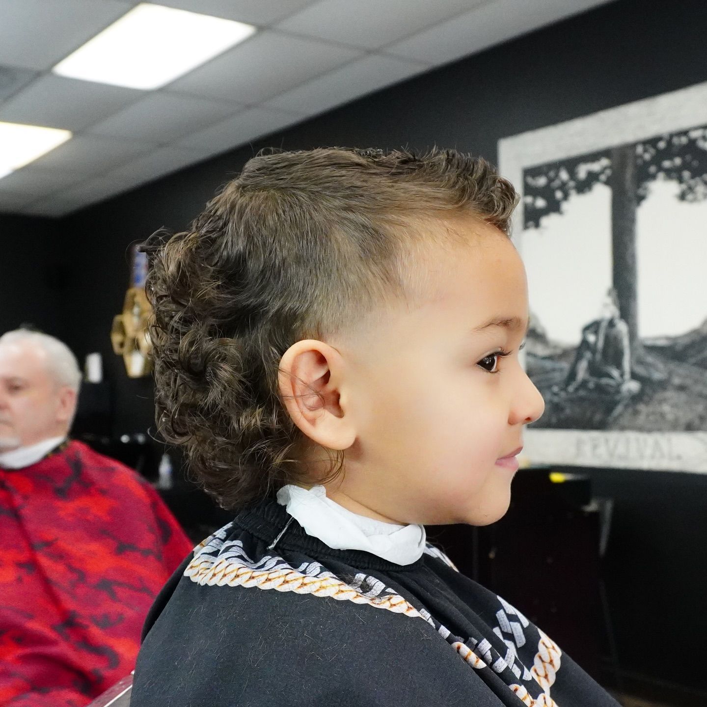 Child in profile wearing a patterned sweater, seated indoors with a framed black-and-white wall art behind them