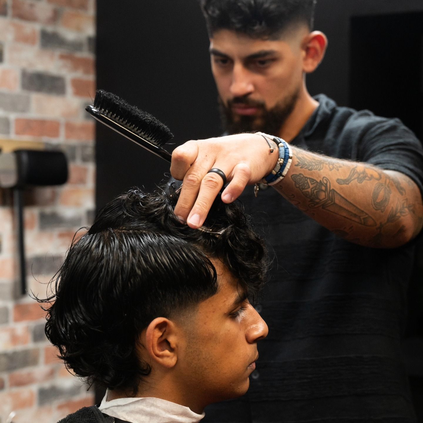 Barber styling a client’s dark hair with comb and scissors in a barbershop