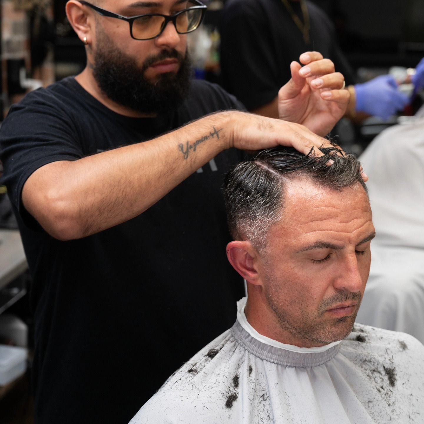 Barber cutting a man’s hair in a salon, with clippings on the cape.