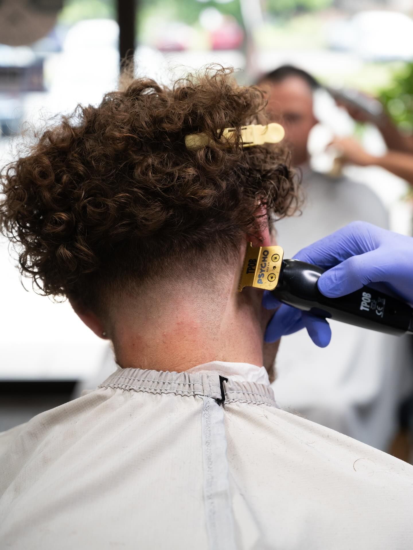 Barber trimming the back of a client’s curly hair with electric clippers