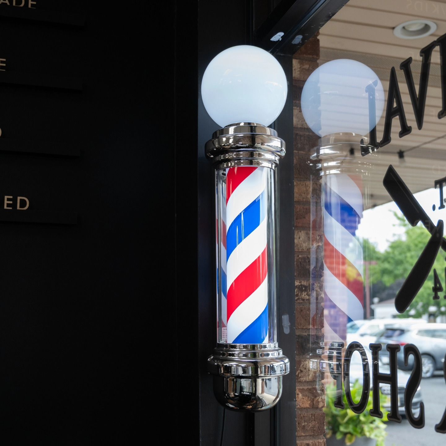 Classic red, white, and blue barber pole on a shop window with the word “BARBER” reflected nearby