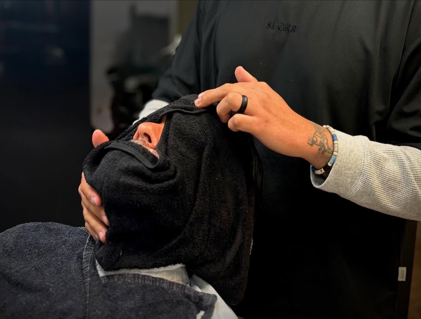 Person getting a head massage while wearing a black towel hood in a salon setting