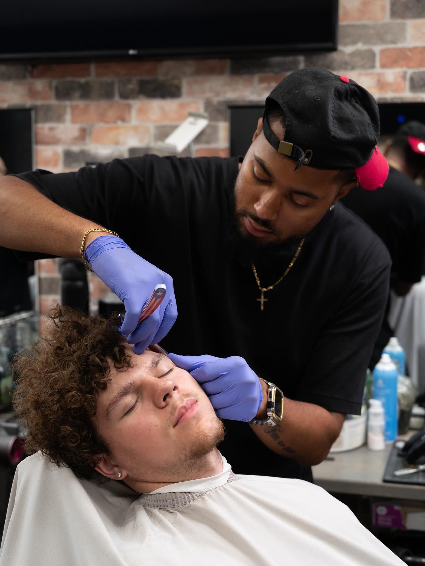 Barber trimming a client's hair in a shop, wearing blue gloves and a black shirt