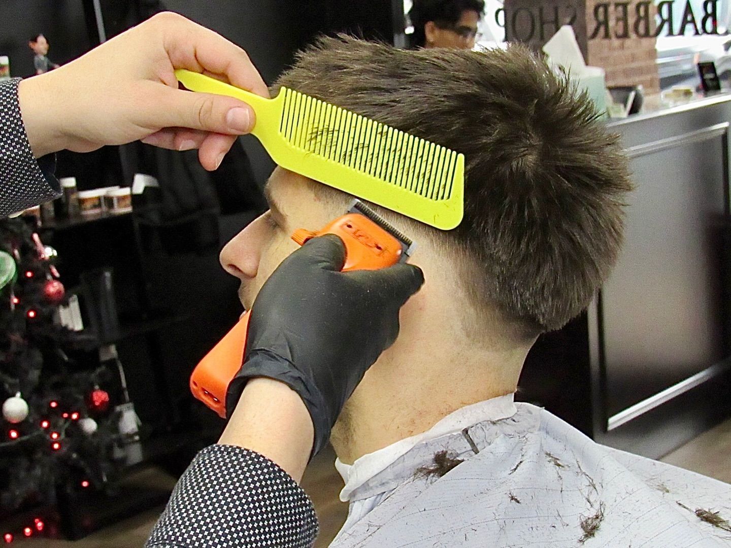 Barber trimming a man's hair with orange clippers and a yellow comb in a salon