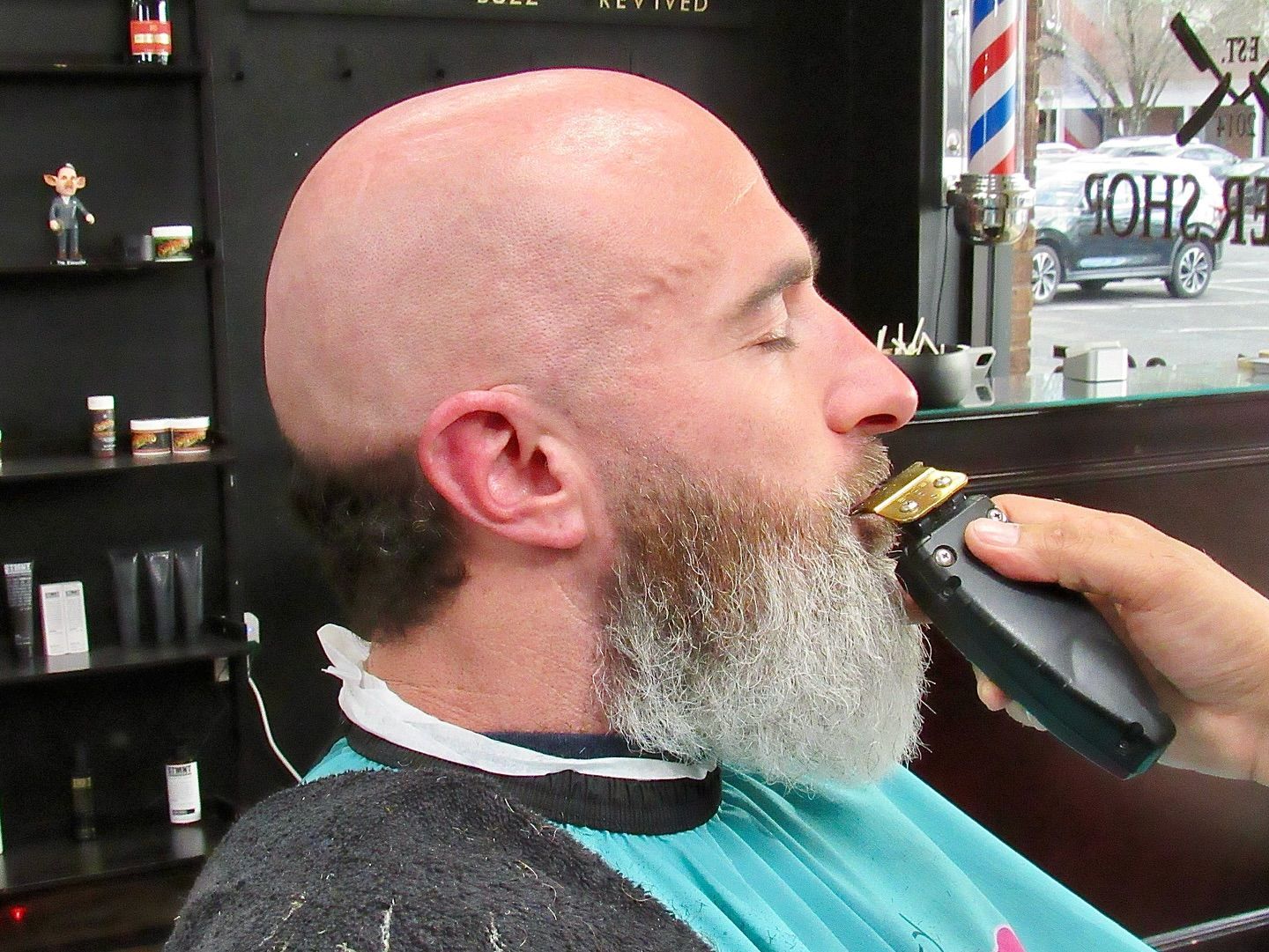 Man getting his beard trimmed with electric clippers in a barbershop