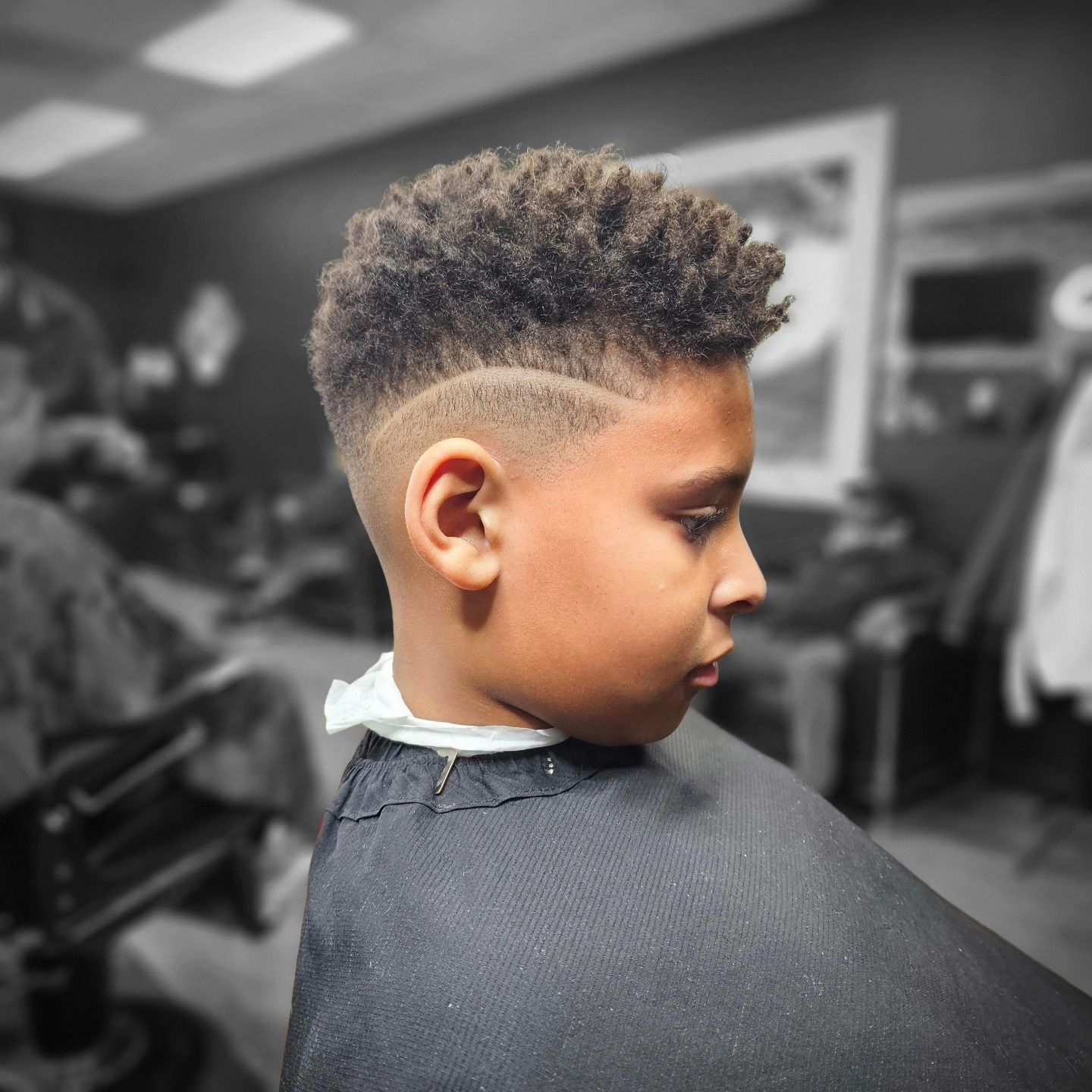 Side-profile haircut with a curly top and shaved fade in a barbershop chair.