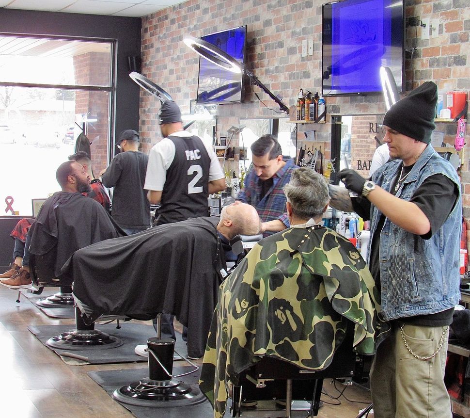 Barbers cutting hair in a busy barbershop with mirrors, chairs, and customers waiting