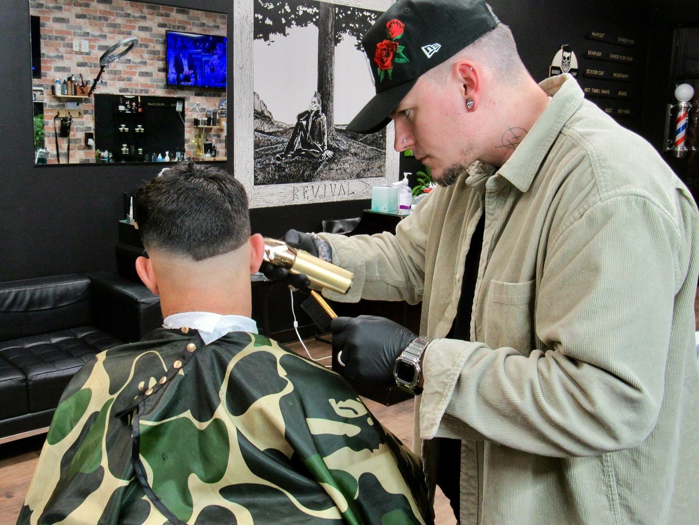Barber cutting a client’s hair in a barbershop, with a camouflage cape and a black glove.