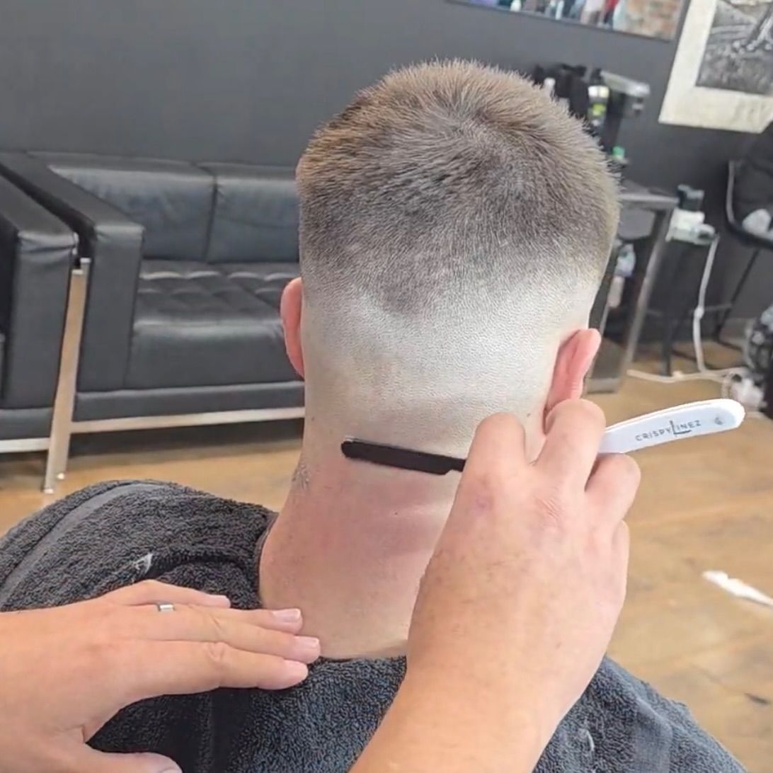 Barber trimming the nape of a short fade haircut in a salon