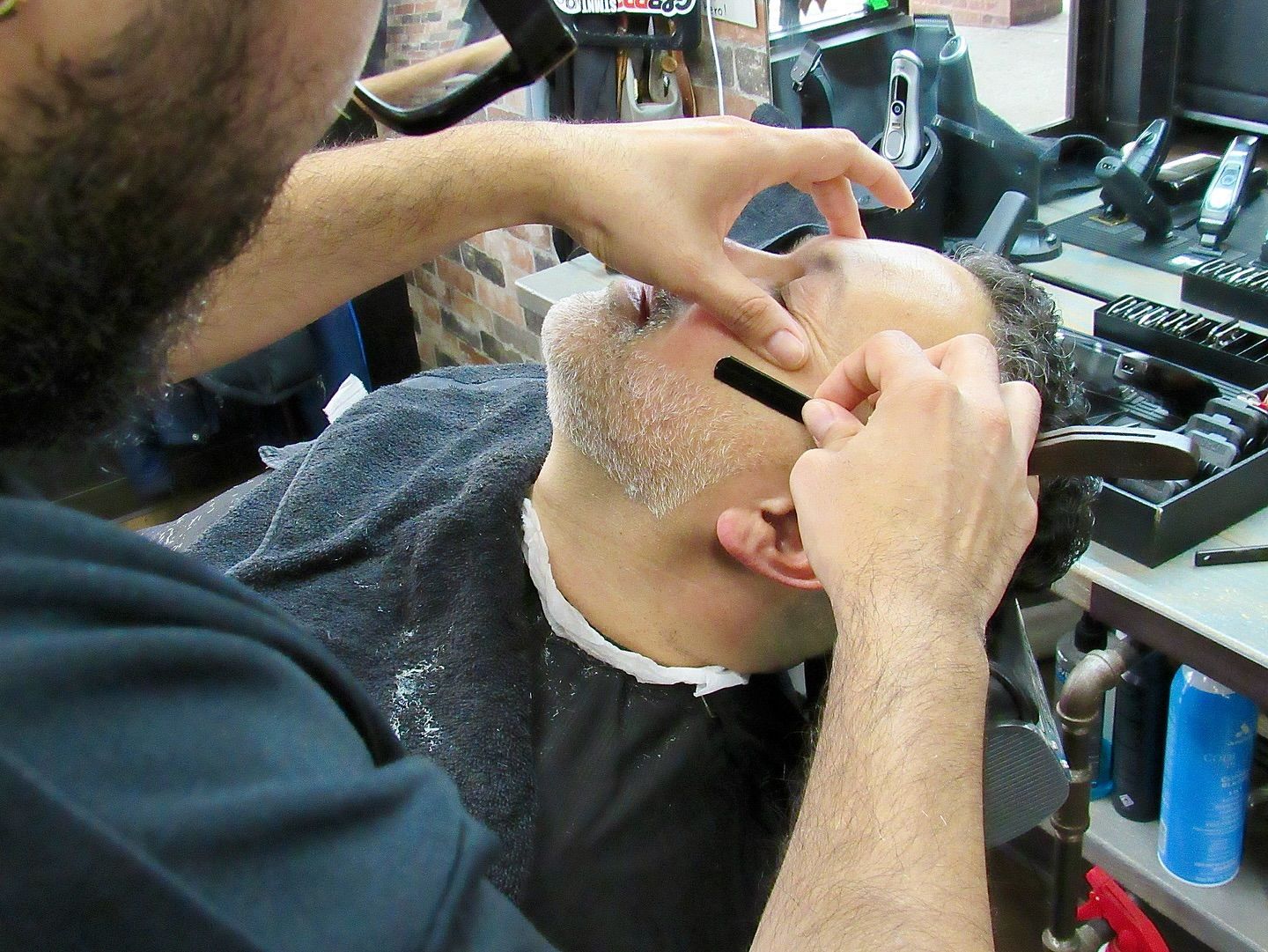 Barber shaving a customer’s head with a straight razor in a shop
