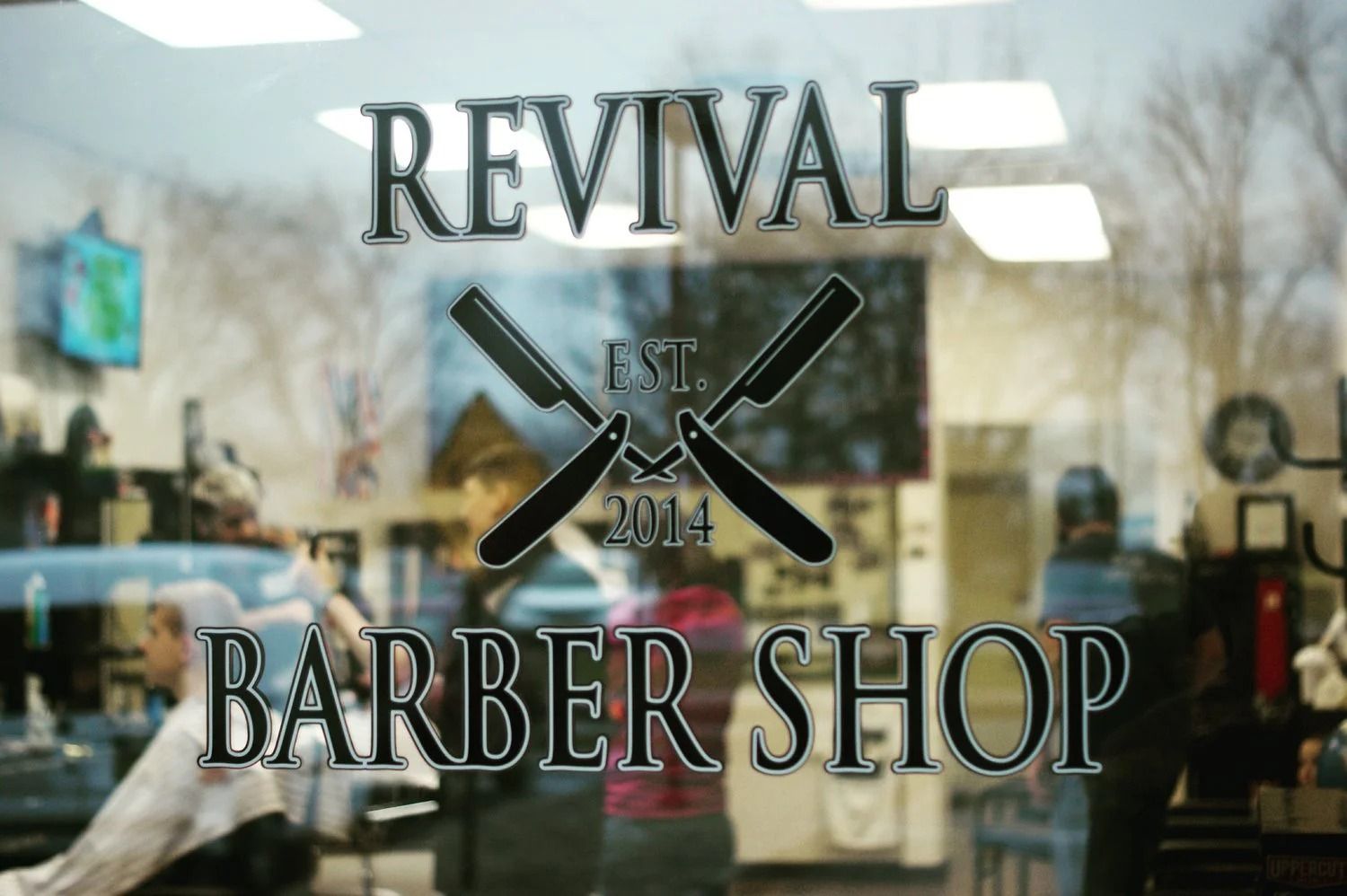 REVIVAL BARBER SHOP sign on glass door with crossed scissors logo and blurred interior behind it