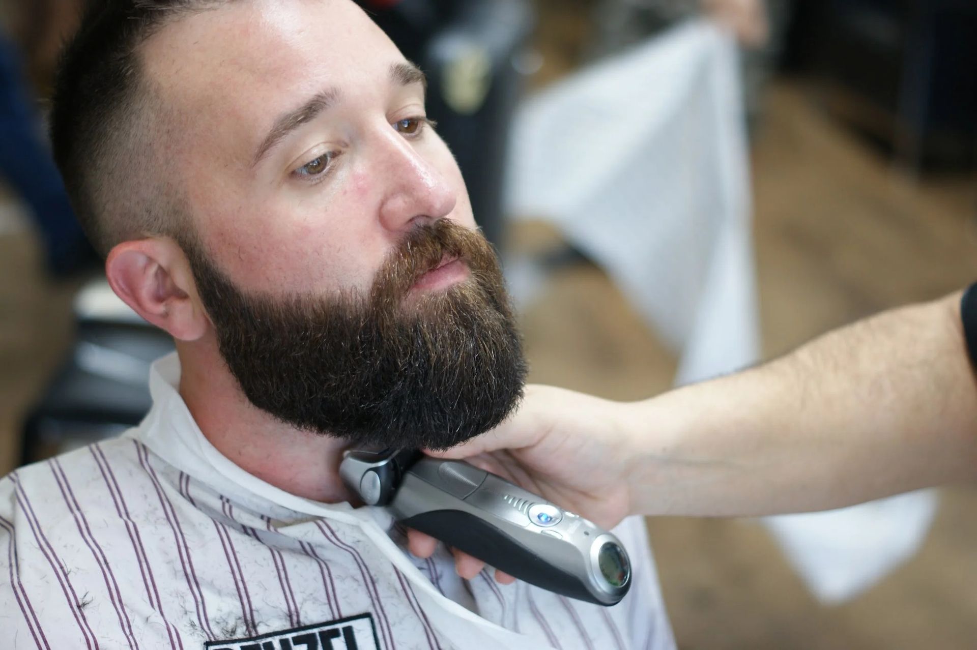 Bearded man getting a haircut while a barber trims his neck with electric clippers