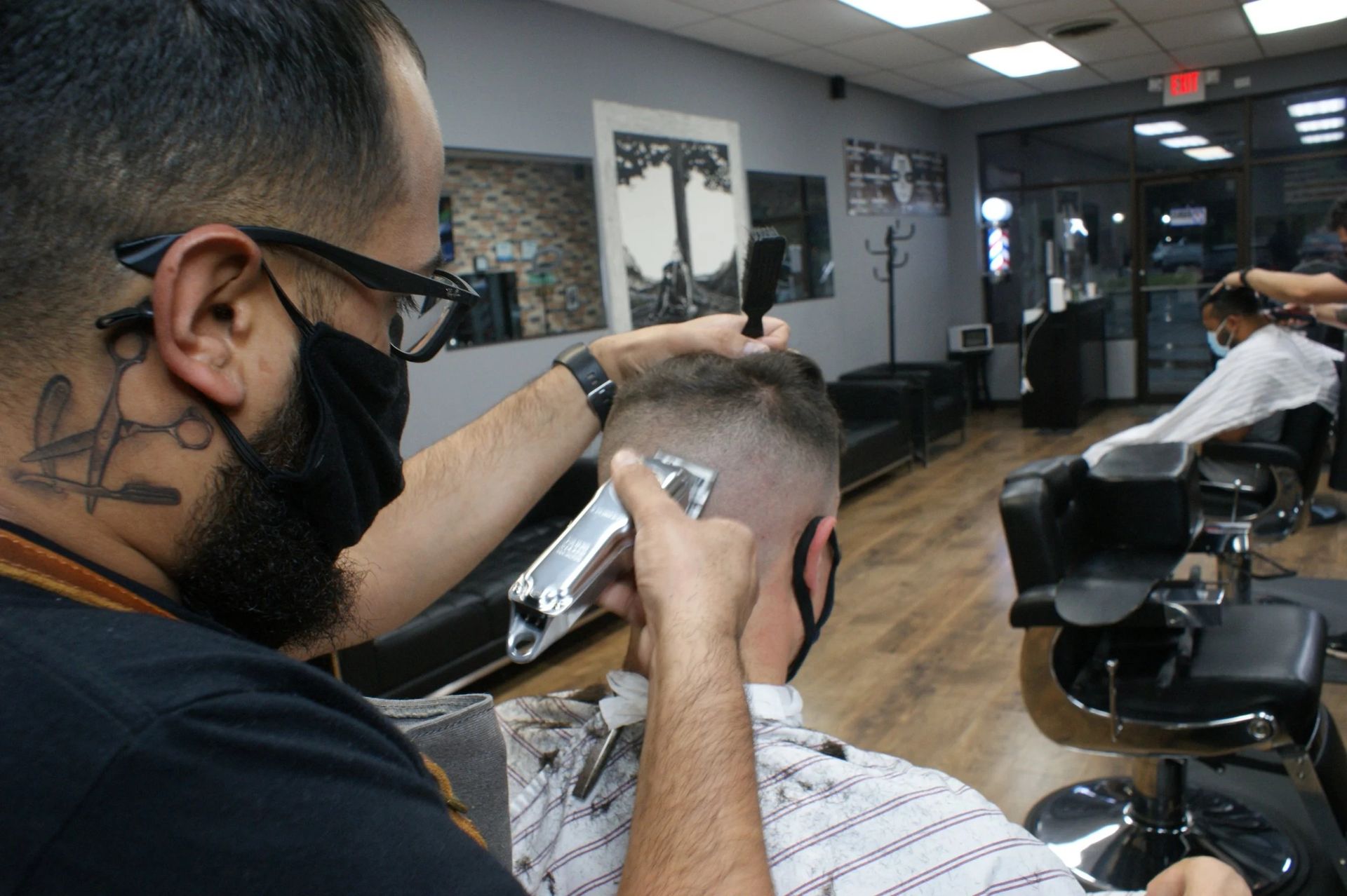 Barber cutting a client’s hair in a modern barbershop, with chairs and mirrors in the background