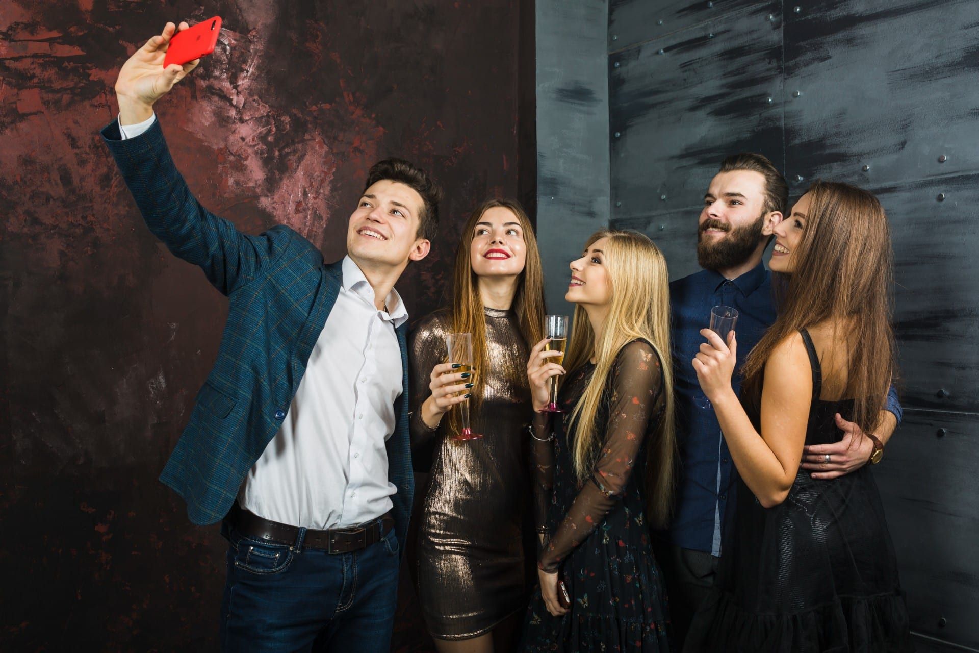 Group of six people posing for a selfie in front of a textured wall; they are holding drinks and smiling.