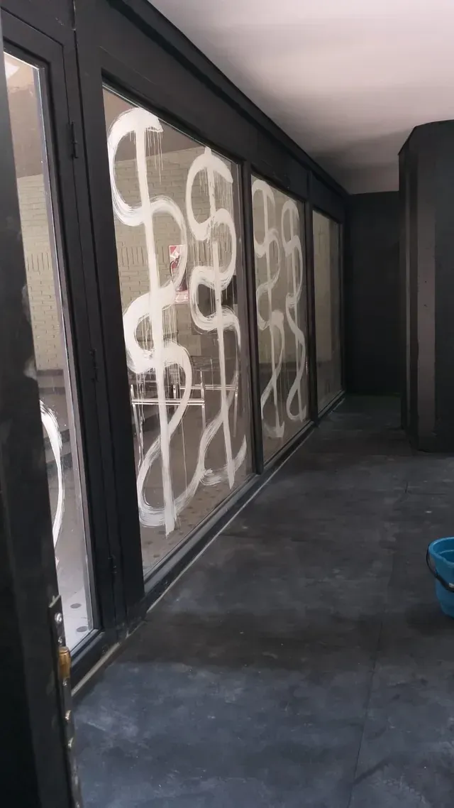 Pasarela cubierta con suelo oscuro y grandes ventanas señalizadas con marcas blancas en forma de X.
